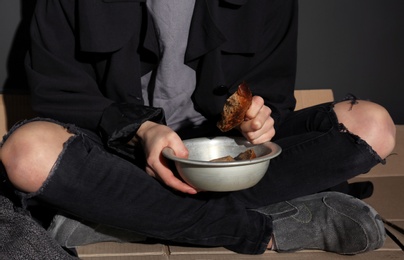 Photo of Poor woman with bread sitting on floor near dark wall, closeup