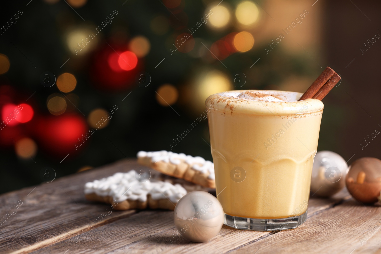 Photo of Tasty eggnog with cinnamon, cookies and baubles on wooden table against blurred festive lights. Space for text