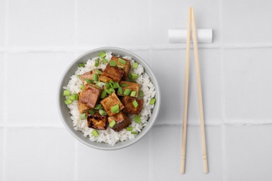 Photo of Bowl of rice with fried tofu and greens on white tiled table, flat lay