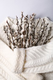 Photo of Beautiful blooming willow branches wrapped in white sweater on light grey background, top view