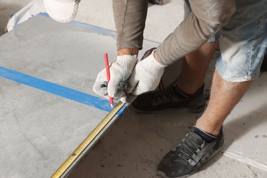 Photo of Worker measuring tiles for installation, closeup view