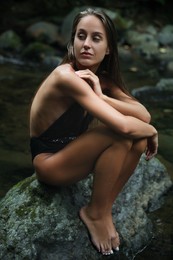 Beautiful young woman sitting on rock near mountain river outdoors