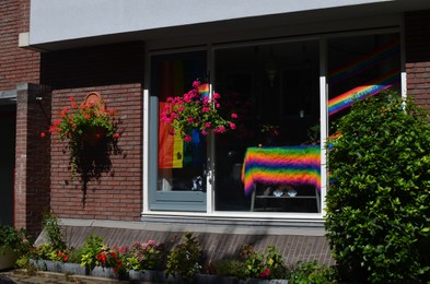 Building facade with flower decor and bright rainbow LGBT pride flags on window, view from outdoors