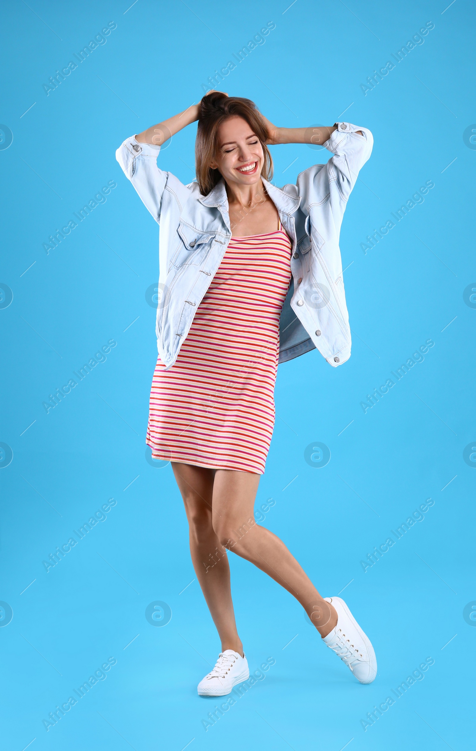 Photo of Beautiful young woman in dress and jacket dancing on blue background