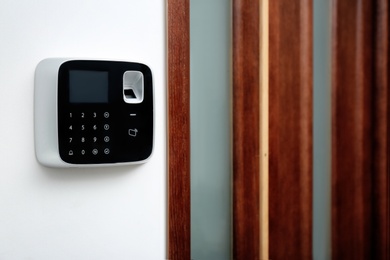 Modern alarm system with fingerprint scanner on white wall indoors. Space for text