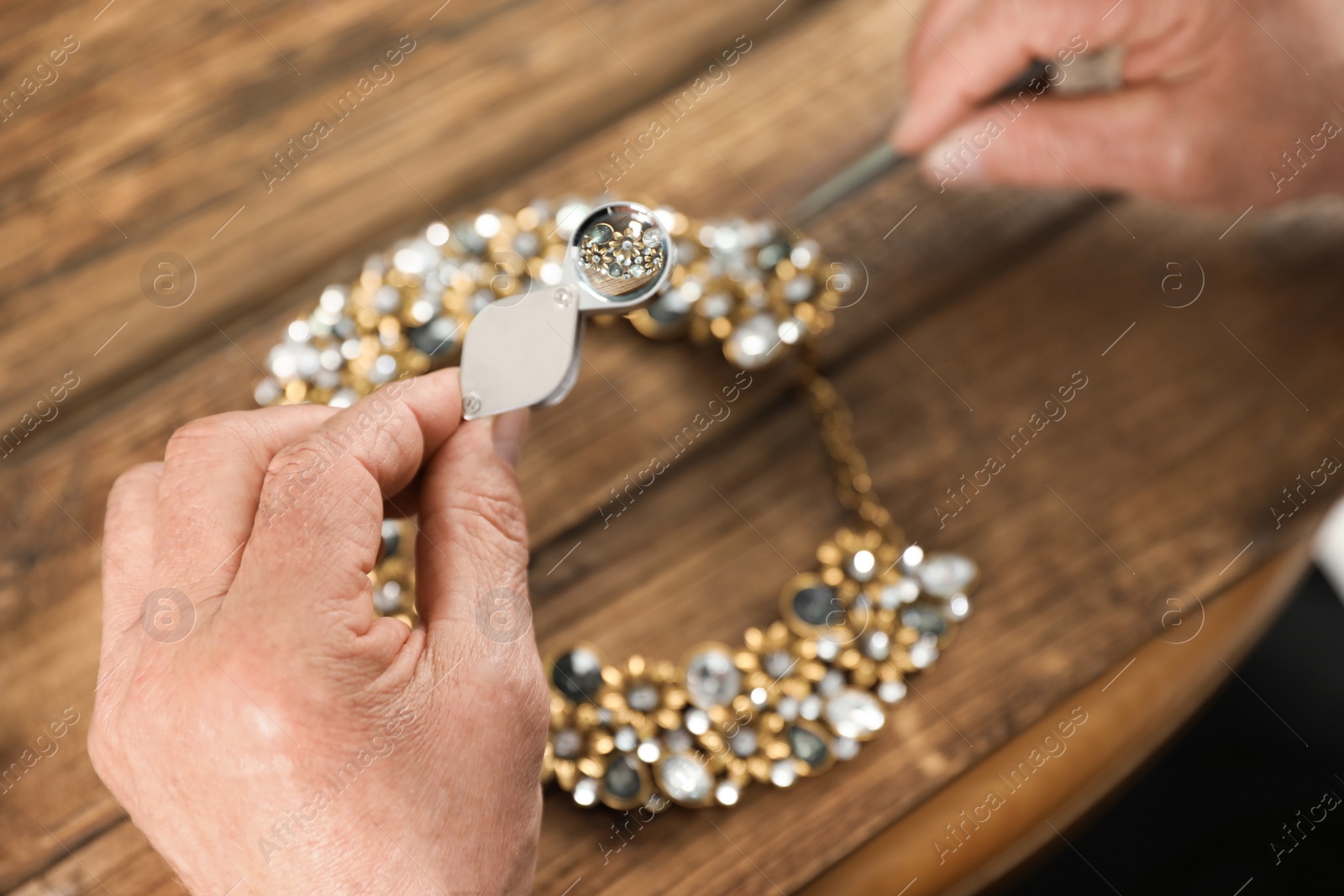 Photo of Male jeweler evaluating necklace at table in workshop, closeup view through magnifier