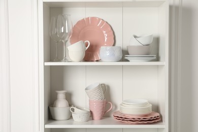 Photo of Different ceramic dishware and glasses on shelves in cabinet indoors