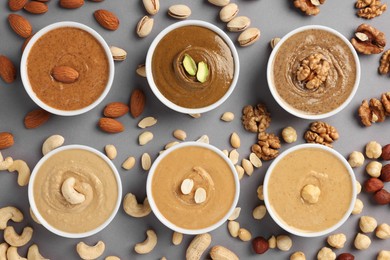 Photo of Many tasty nut butters in bowls and nuts on grey table, flat lay