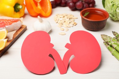 Paper cutout of kidneys and different products on white wooden table
