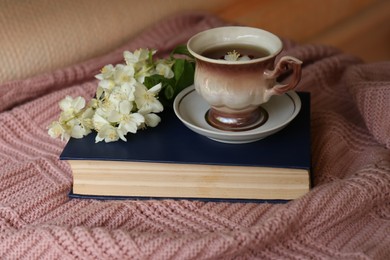 Photo of Cup of aromatic tea with beautiful jasmine flowers and book on pink fabric