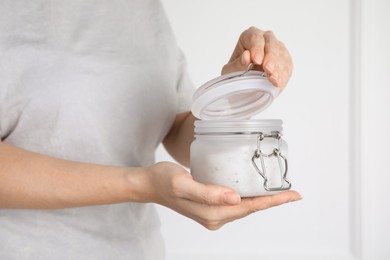 Woman holding jar of salt scrub on light background, closeup