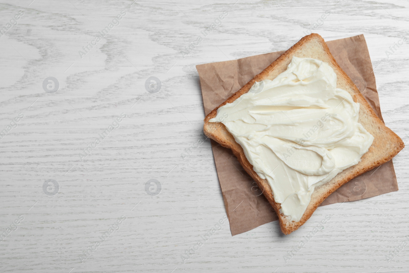 Photo of Slice of bread with tasty cream cheese on white wooden table, top view. Space for text