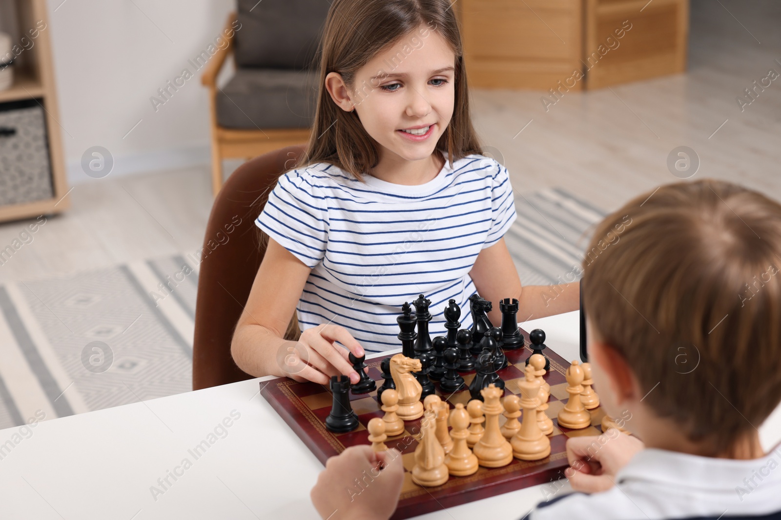 Photo of Cute children playing chess at table in room