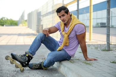 Photo of Handsome young man with inline roller skates sitting on curb outdoors
