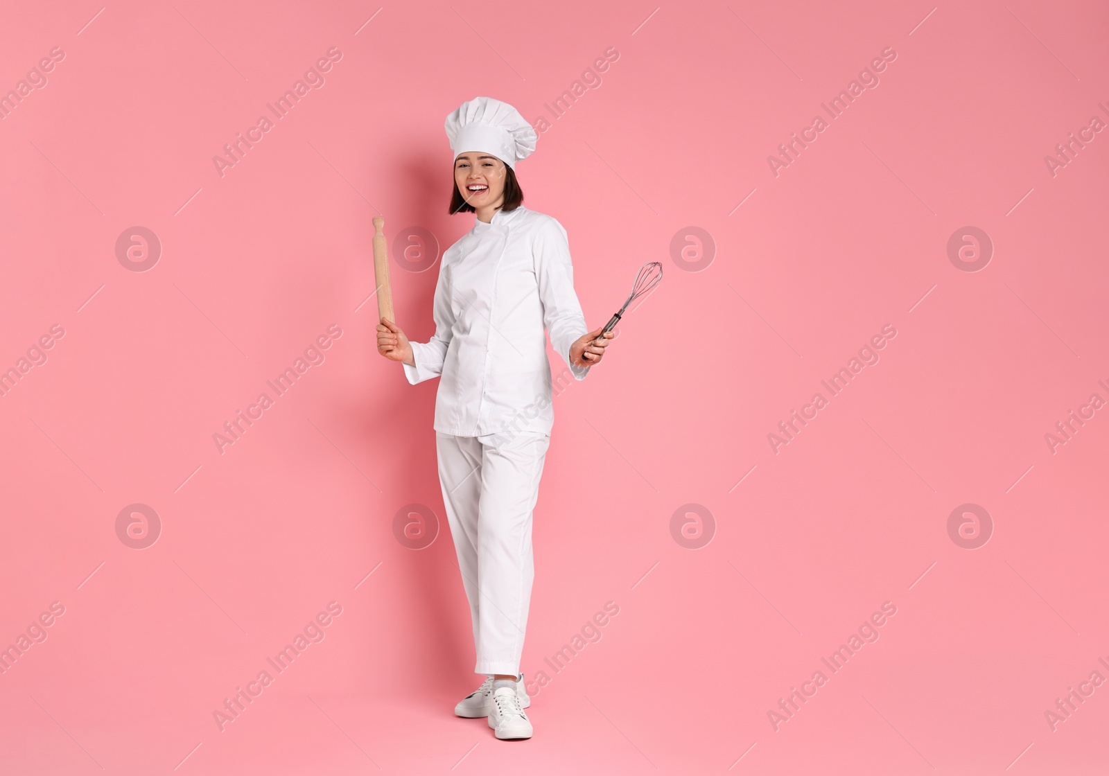 Photo of Happy confectioner with rolling pin and whisk on pink background