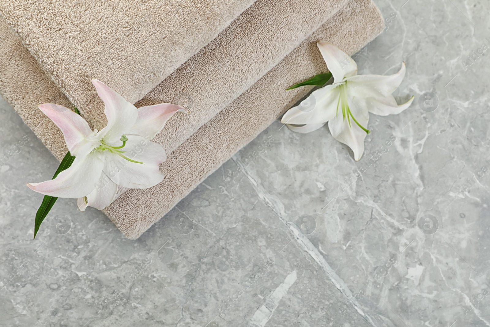 Photo of Stack of fresh towels with flowers on grey table, top view. Space for text