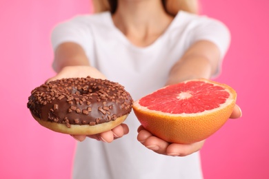 Photo of Woman choosing between doughnut and healthy grapefruit on pink background, closeup