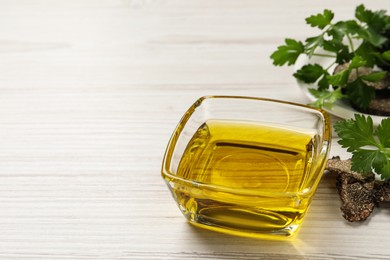 Photo of Fresh truffle oil in glass bowl and parsley on white wooden table, space for text