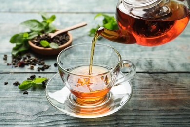 Photo of Pouring black tea into glass cup on wooden table