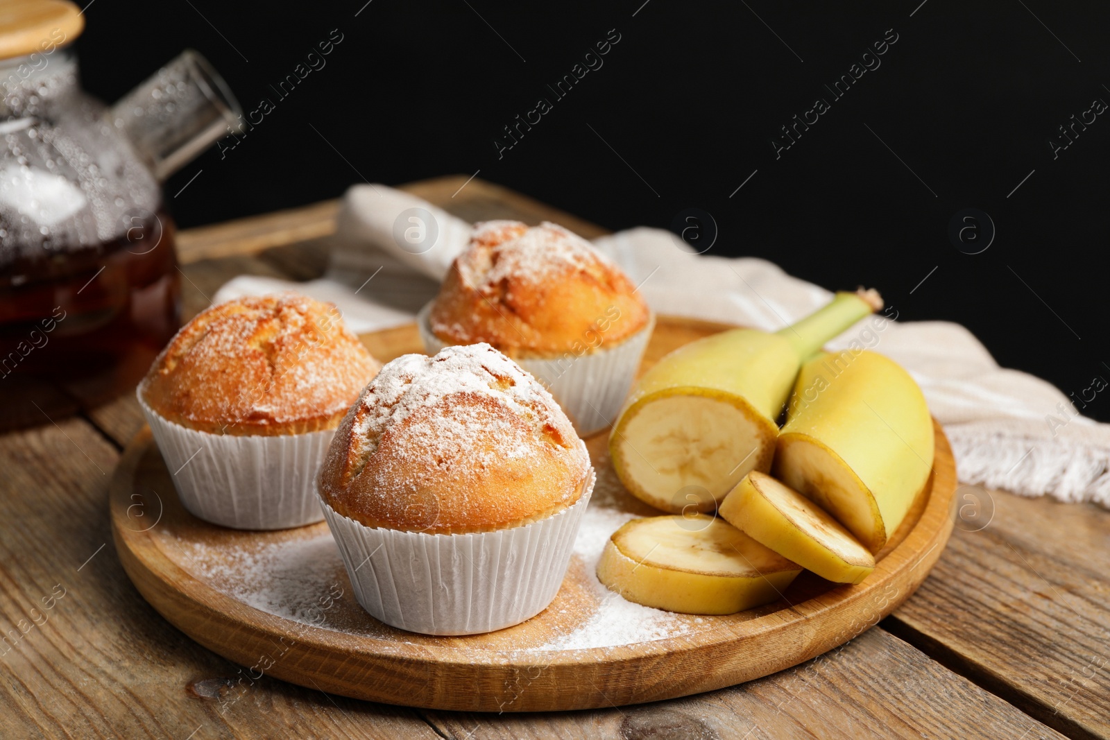 Photo of Tasty muffins served with banana slices on wooden table against dark background