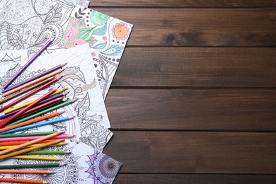 Photo of Antistress coloring pages and pencils on wooden table, flat lay. Space for text