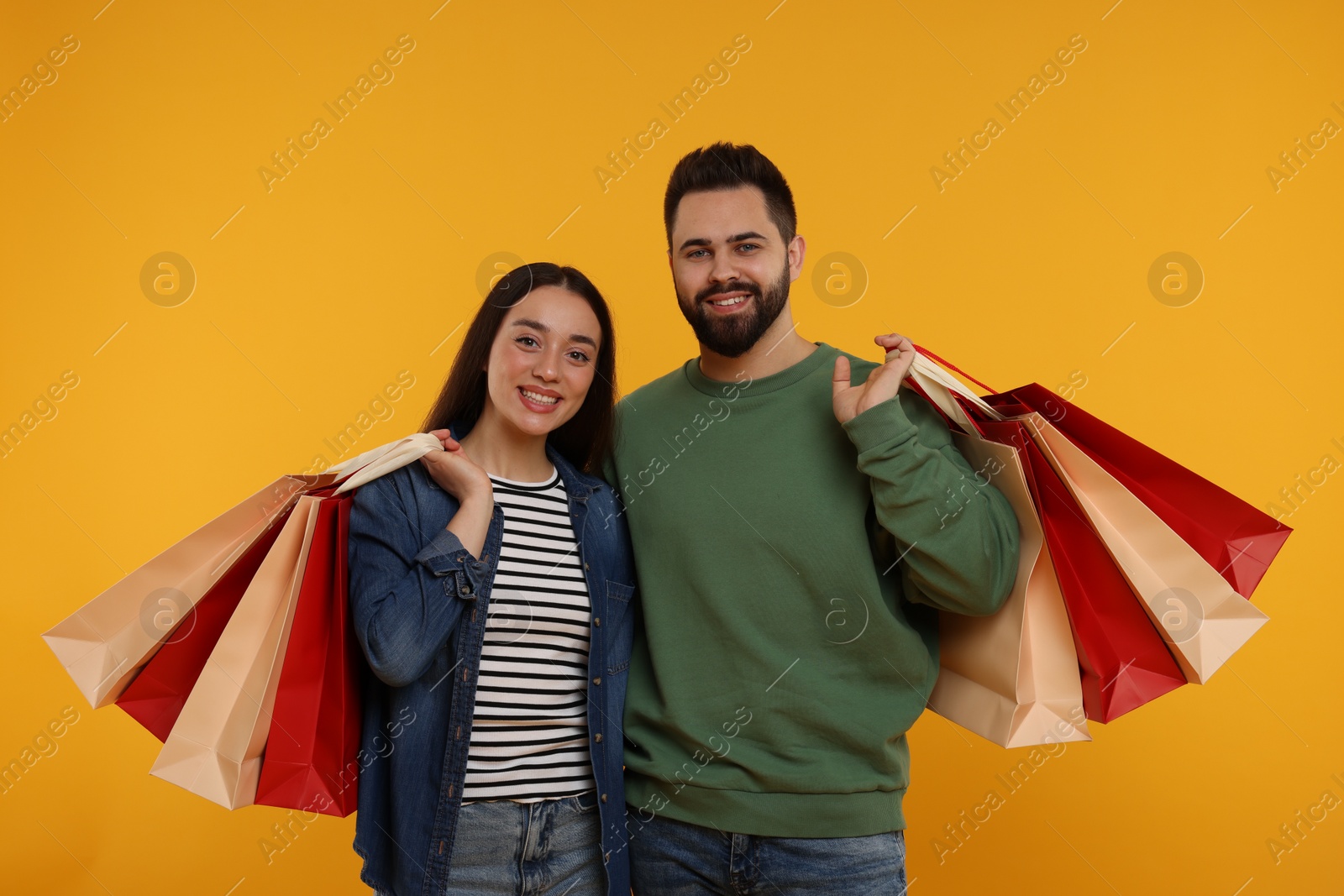 Photo of Happy couple with shopping bags on orange background