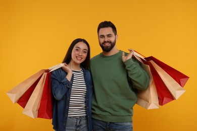 Happy couple with shopping bags on orange background