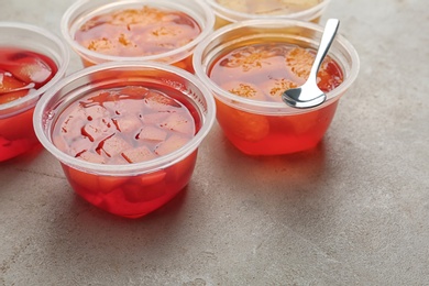 Photo of Plastic containers with tasty jelly desserts on grey table