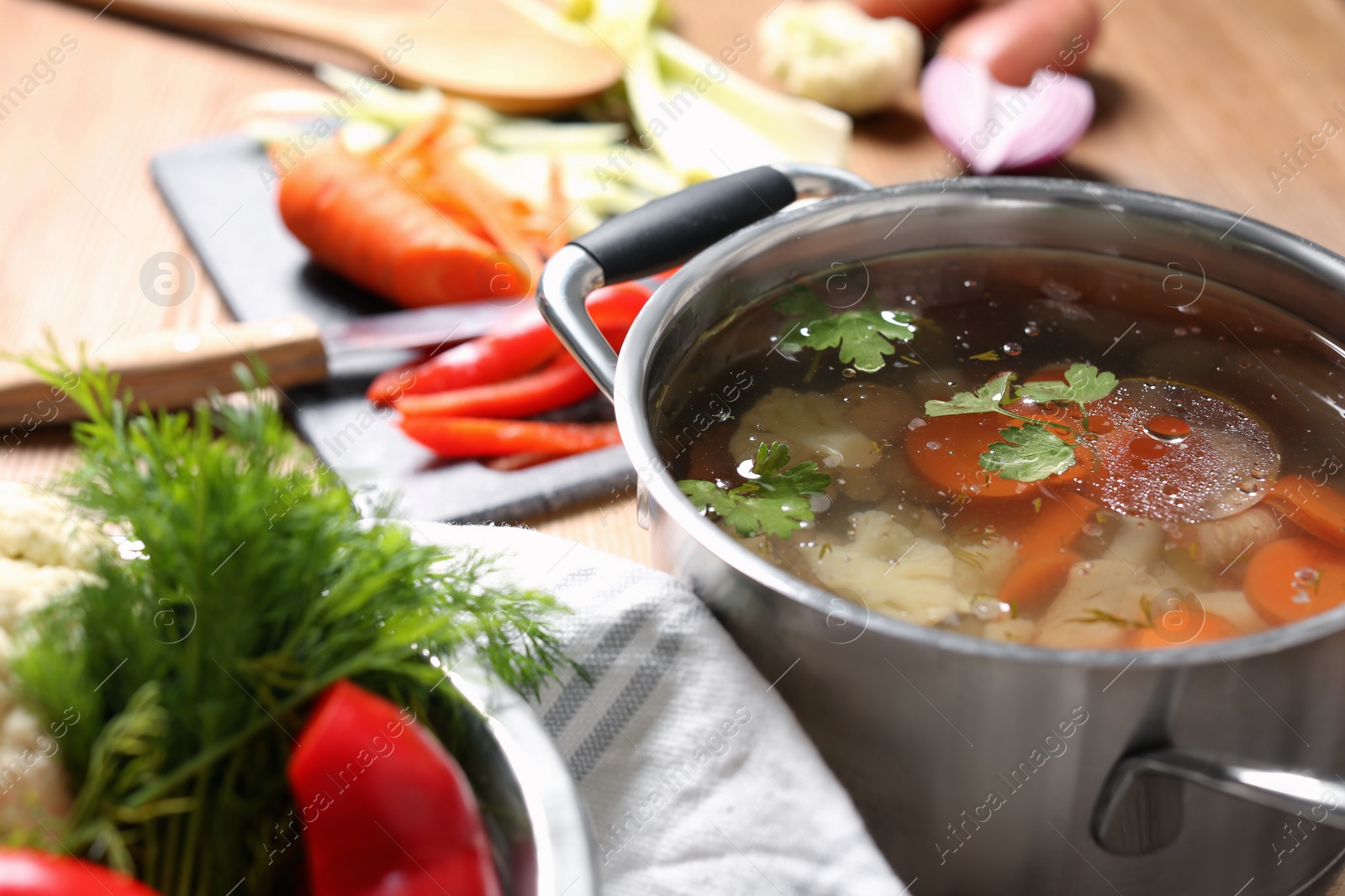 Photo of Pot of delicious vegetable bouillon and ingredients on table, closeup