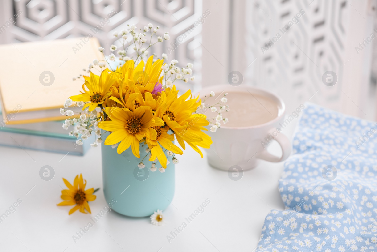 Photo of Beautiful bright flowers, cup of coffee and fabric on white table. Space for text