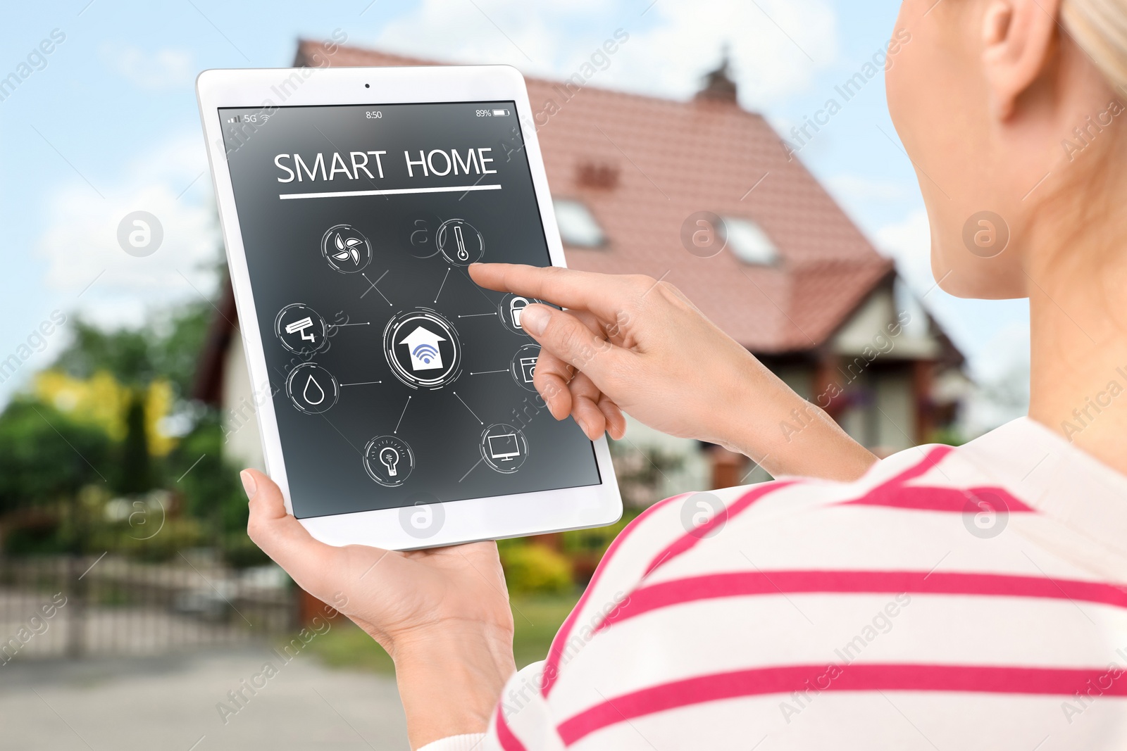 Image of Woman using smart home control system via tablet near house outdoors, closeup