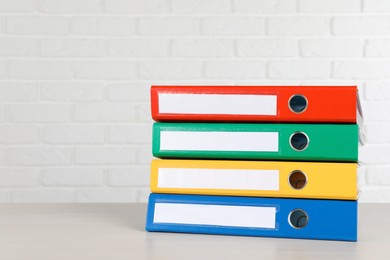 Stack of office folders on wooden table near white brick wall, space for text