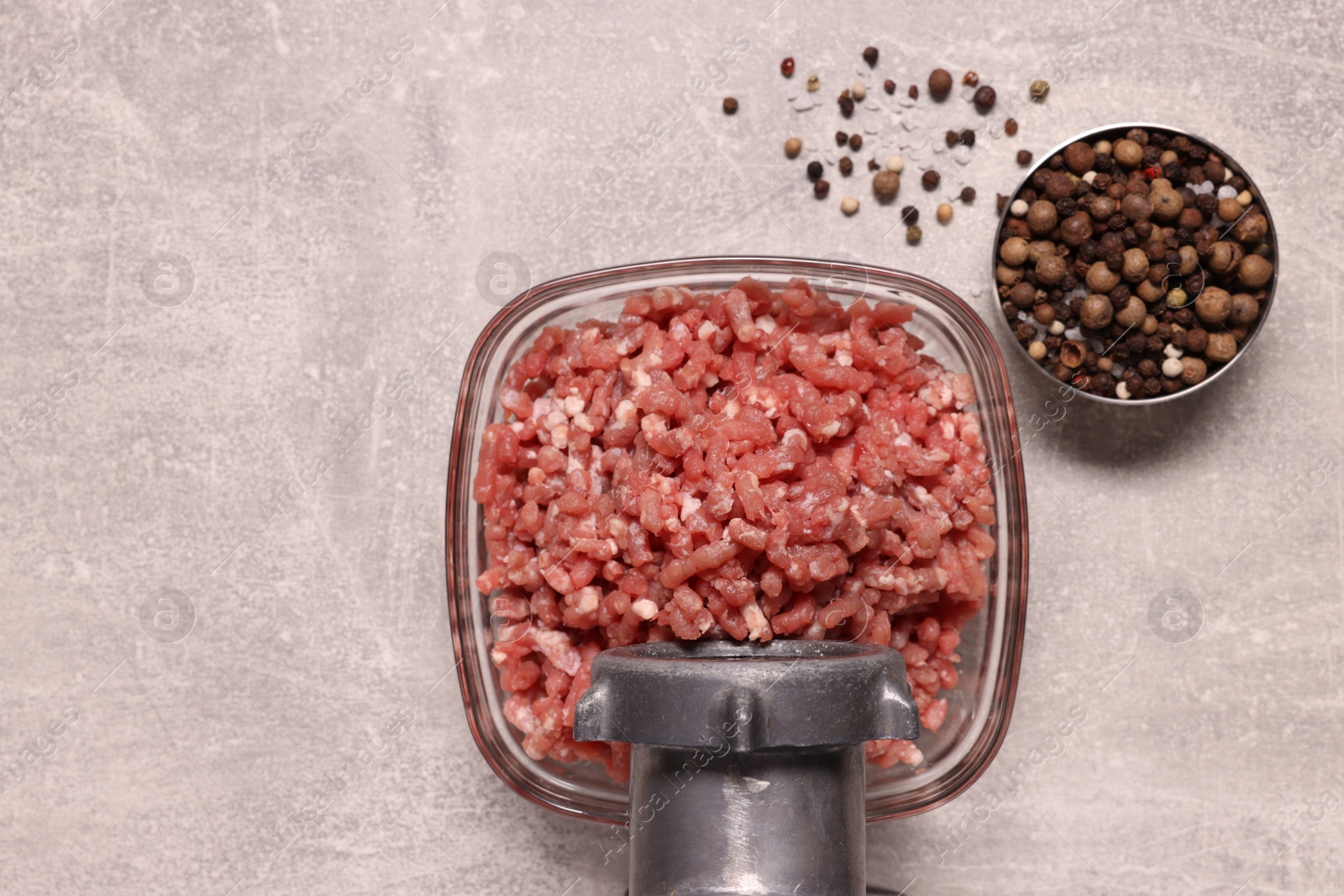 Photo of Manual meat grinder with beef mince and peppercorns on light grey table, flat lay. Space for text