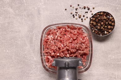Photo of Manual meat grinder with beef mince and peppercorns on light grey table, flat lay. Space for text
