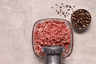 Manual meat grinder with beef mince and peppercorns on light grey table, flat lay. Space for text