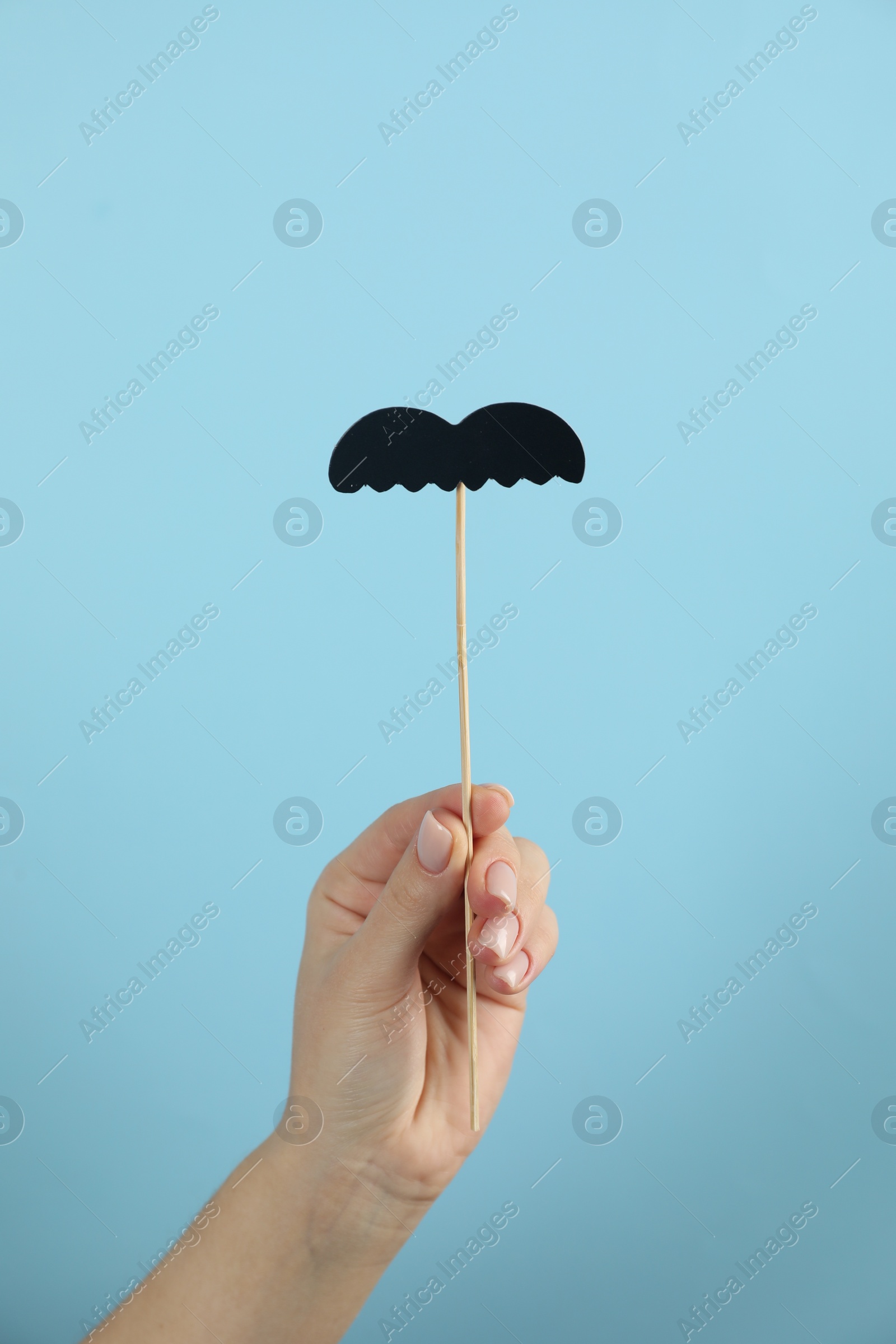 Photo of Woman with fake paper mustache on light blue background, closeup