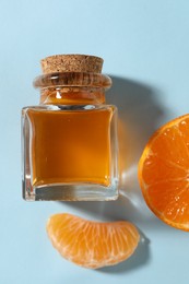 Photo of Aromatic tangerine essential oil in bottle and citrus fruit on light blue table, top view