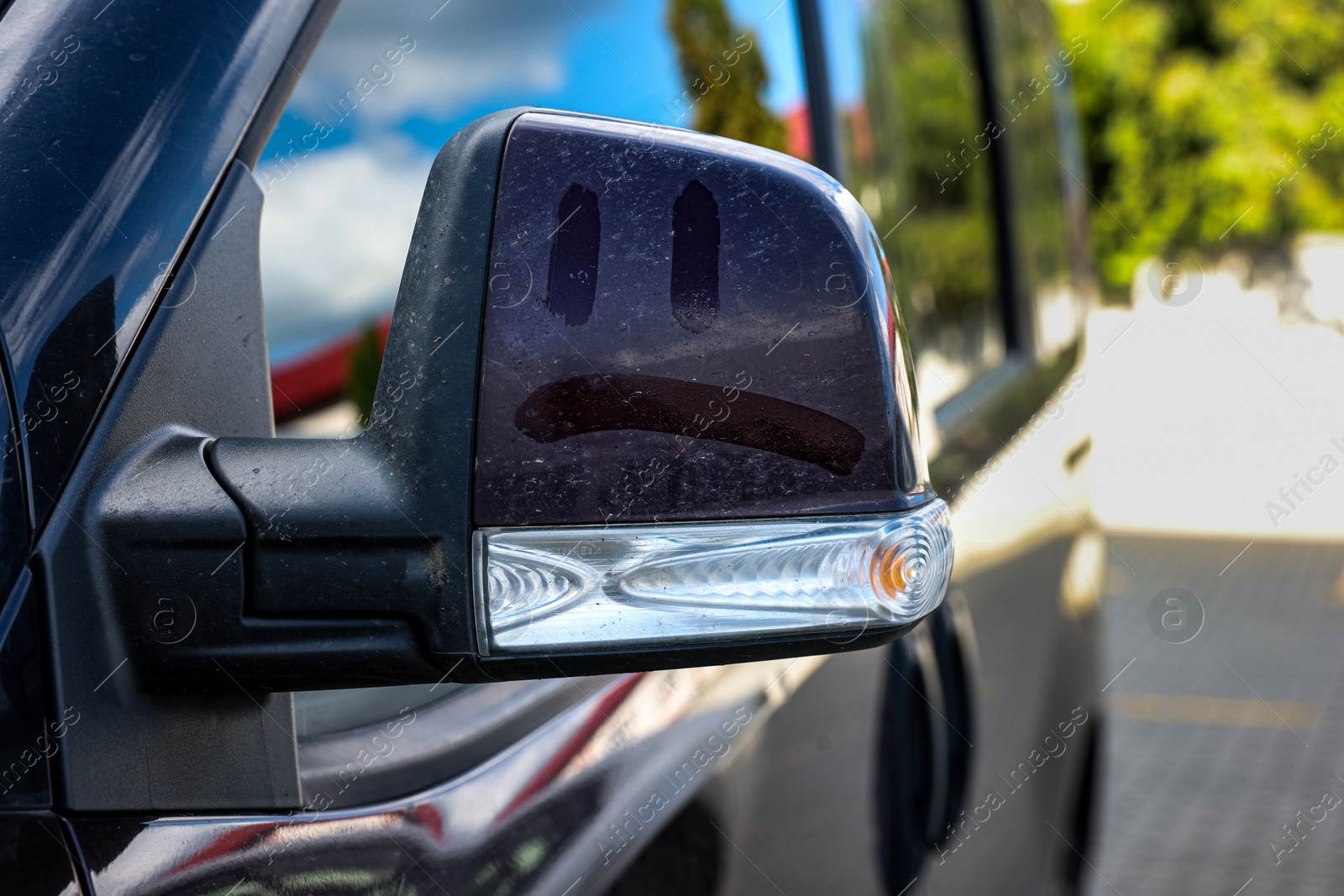 Photo of Sad smiley on dirty side view mirror of car outdoors, closeup
