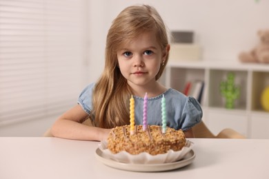 Photo of Cute girl with birthday cake at table indoors
