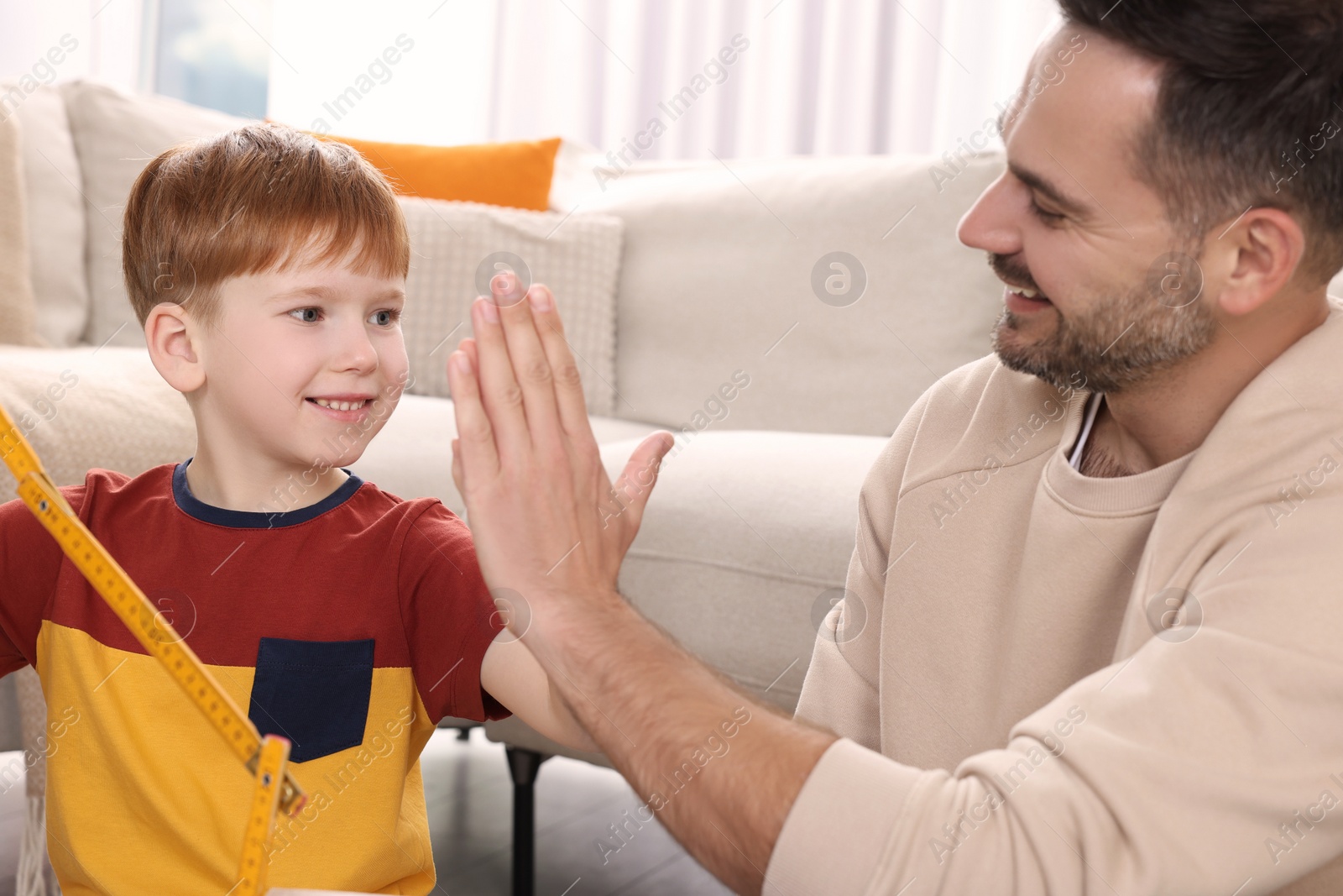 Photo of Son giving five to father near sofa at home. Repair work