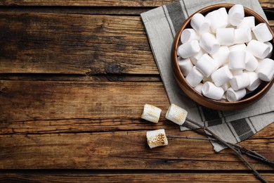 Sticks with roasted marshmallows on wooden table, flat lay. Space for text