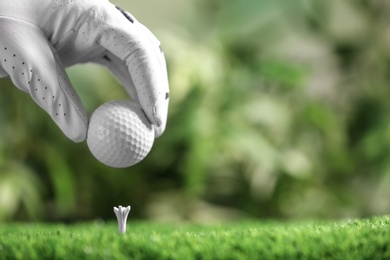 Photo of Player putting golf ball on tee against blurred background, closeup. Space for text