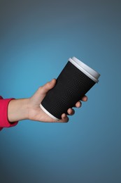 Woman holding takeaway paper coffee cup on blue background, closeup