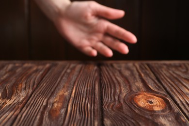 Photo of Woman holding hand above wooden table, selective focus. Space for text