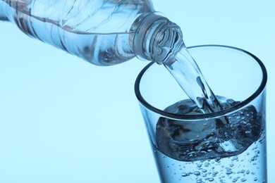 Photo of Pouring water from bottle into glass on light blue background, closeup