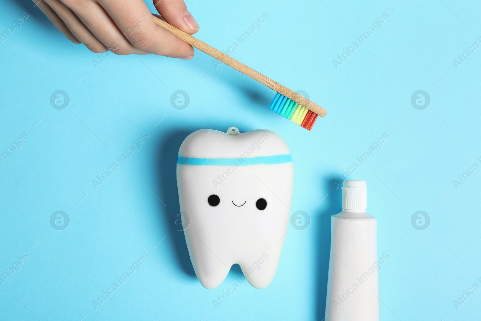 Photo of Woman holding wooden brush near model of tooth and paste on color background, top view