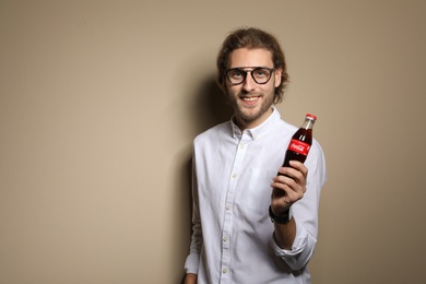 MYKOLAIV, UKRAINE - NOVEMBER 28, 2018: Young man with bottle of Coca-Cola on color background, space for text