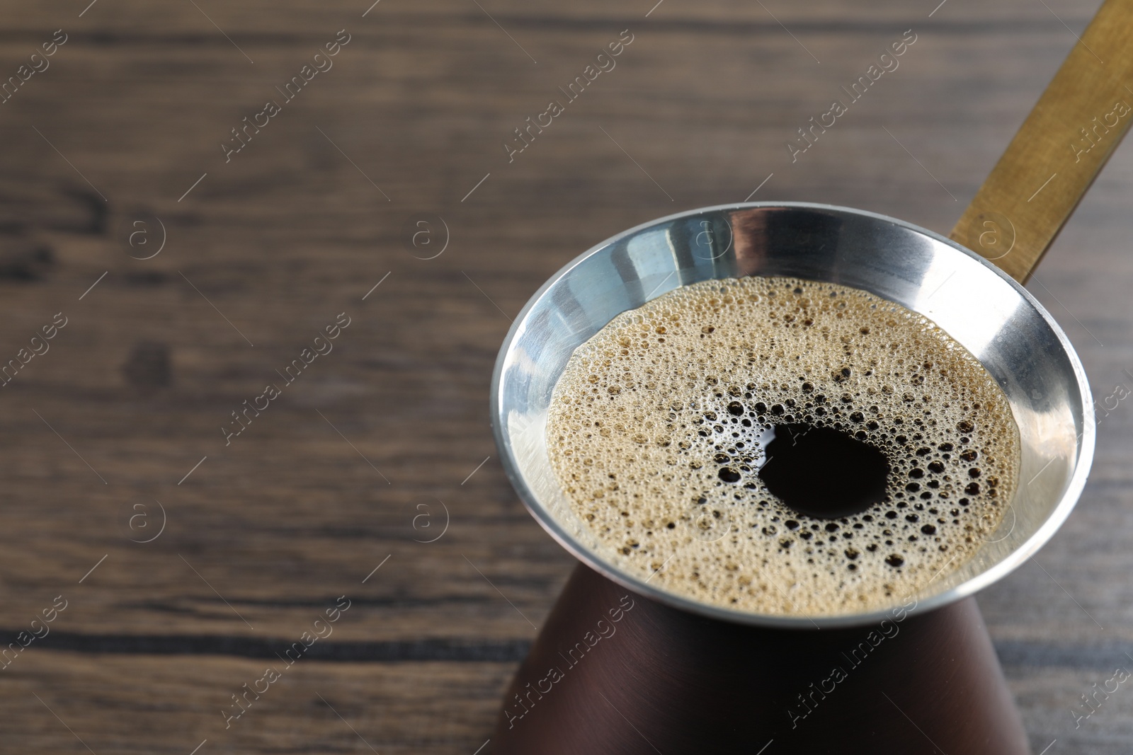 Photo of Turkish coffee pot with hot drink on wooden table, closeup. Space for text