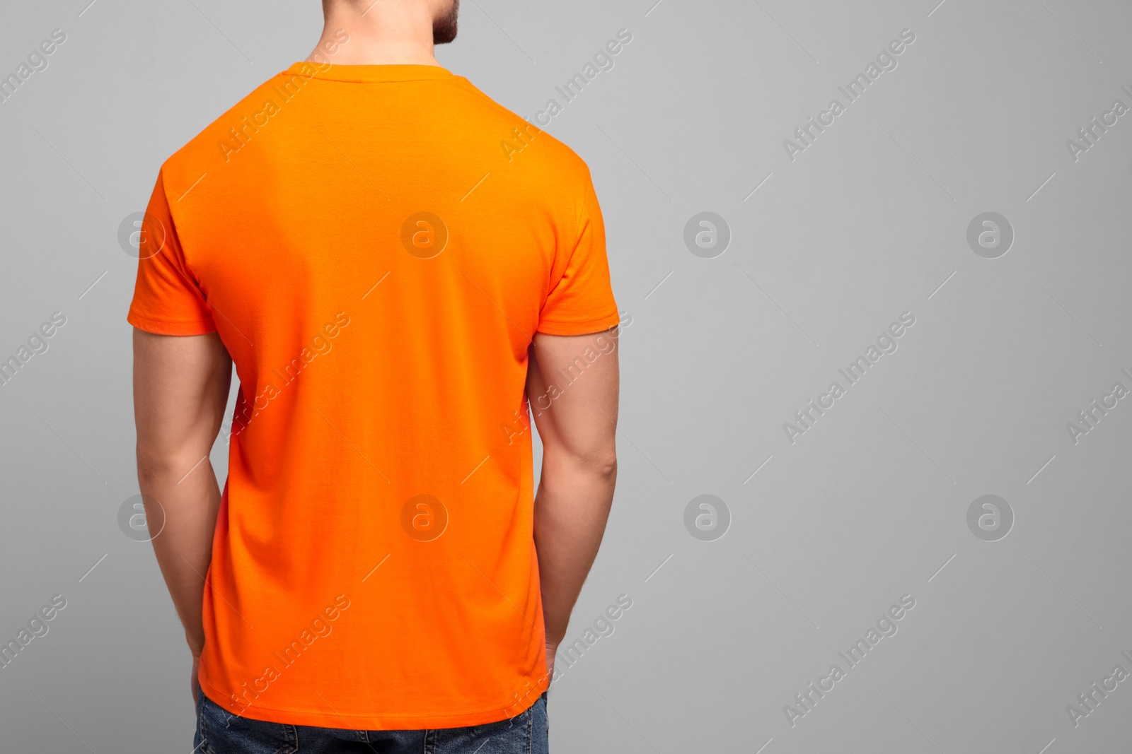 Photo of Man wearing orange t-shirt on light grey background, back view. Mockup for design