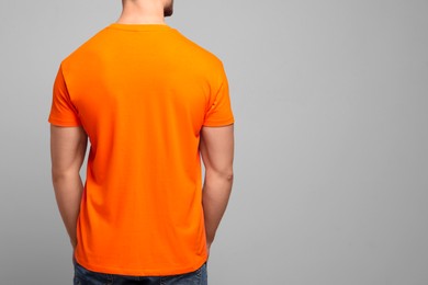 Photo of Man wearing orange t-shirt on light grey background, back view. Mockup for design